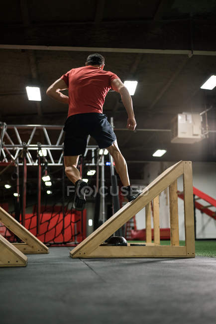Rear view of muscular man jumping on inclined wedges in gym — Stock Photo
