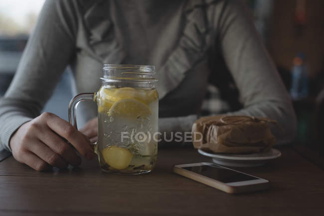 Средняя секция женщины пьет лимонный чай в кафе — стоковое фото