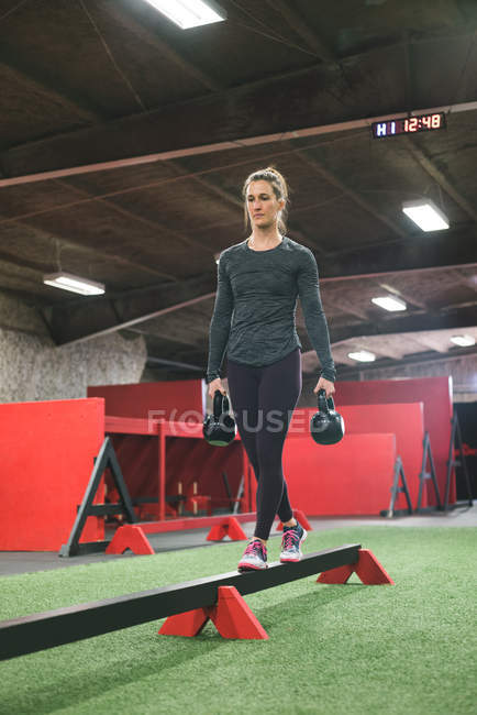 Muskulöse Frau wacht mit Kettlebell auf Balancierbalken auf — Stockfoto