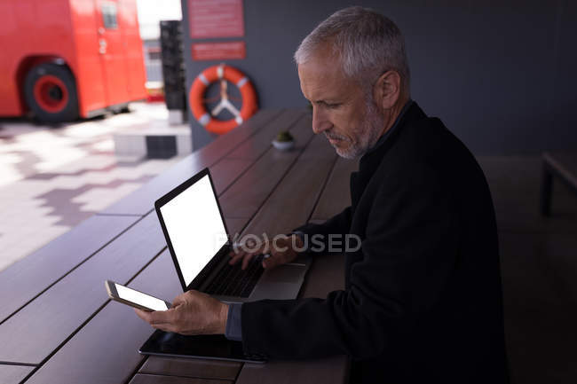 Empresário usando telefone celular enquanto trabalhava em laptop no hotel — Fotografia de Stock