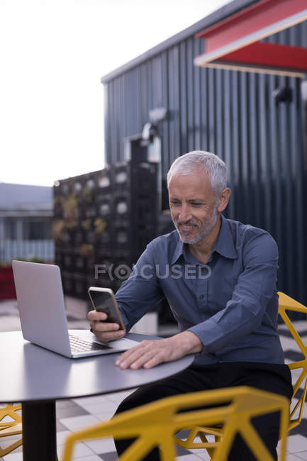 Businessman using mobile phone while working on laptop in hotel premises — Stock Photo
