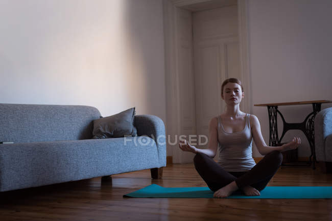 Young woman meditating in yoga posture at home — Stock Photo