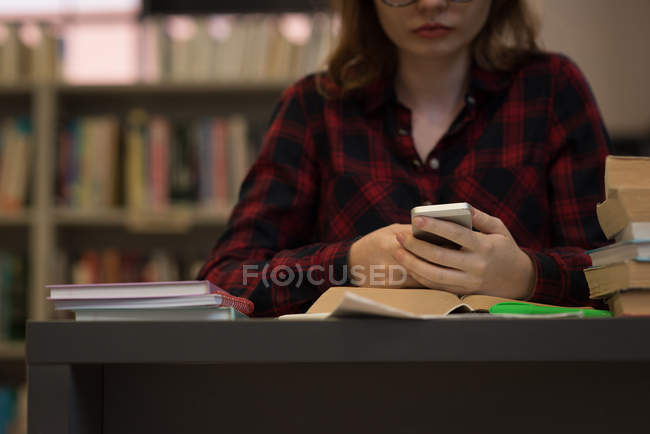 Jeune femme utilisant un téléphone intelligent dans la bibliothèque — Photo de stock