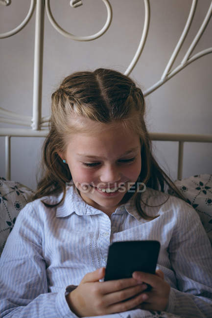 Menina bonito usando telefone celular na cama em casa — Fotografia de Stock