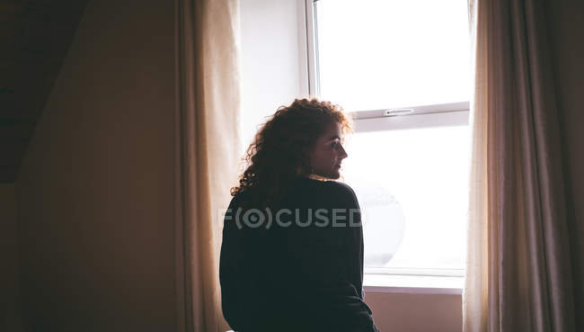 Rear view of thoughtful woman standing near window at home — Stock Photo