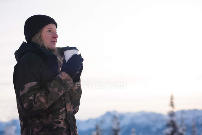 Mulher sorridente com café olhando para montanhas cobertas de neve — Fotografia de Stock