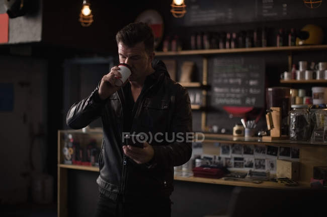 Механік, який використовує мобільний телефон, маючи каву в гаражі — стокове фото