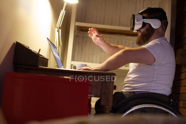 Инвалид в гарнитуре виртуальной реальности использует ноутбук дома — стоковое фото