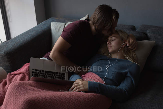 Mann küsst Frau im heimischen Wohnzimmer auf die Stirn — Stockfoto