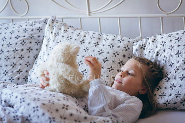 Ragazza che gioca con orsacchiotto sul letto in camera da letto — Foto stock