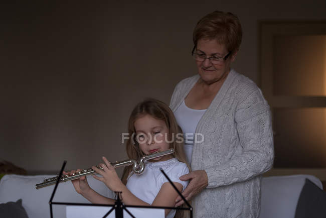 Дівчина грає на флейті зі своєю бабусею у вітальні вдома — стокове фото