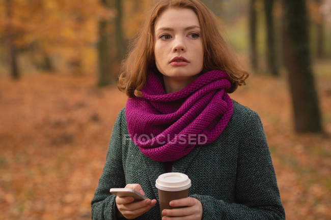 Mulher usando telefone celular enquanto toma café no parque — Fotografia de Stock