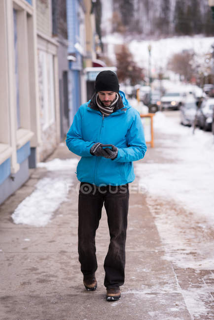 Man using mobile phone while walking on sidewalk during winter — Stock Photo