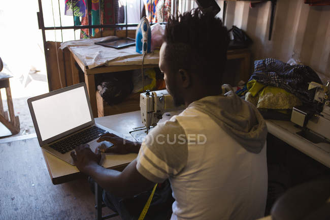 Visão traseira do alfaiate usando laptop na loja — Fotografia de Stock