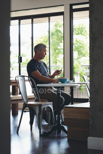 Businessman using mobile phone while having breakfast in office — Stock Photo