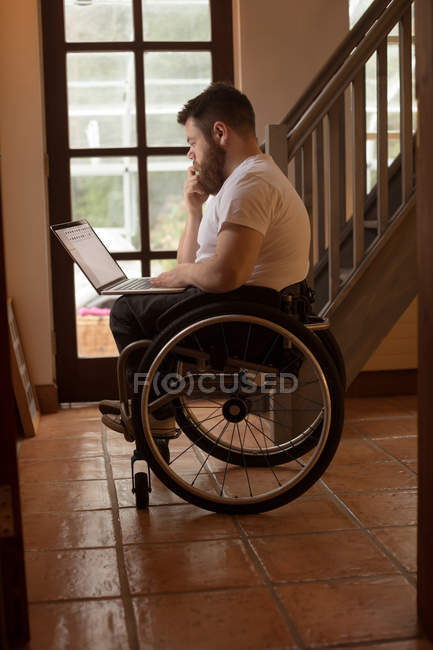 Hombre joven discapacitado usando el ordenador portátil en casa - foto de stock