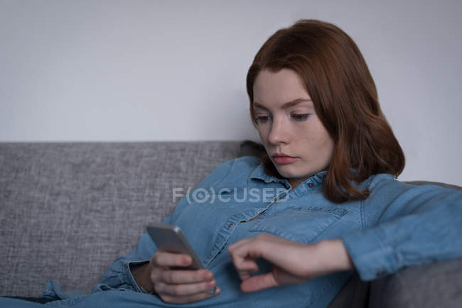 Jeune femme utilisant un téléphone intelligent dans le salon à la maison — Photo de stock