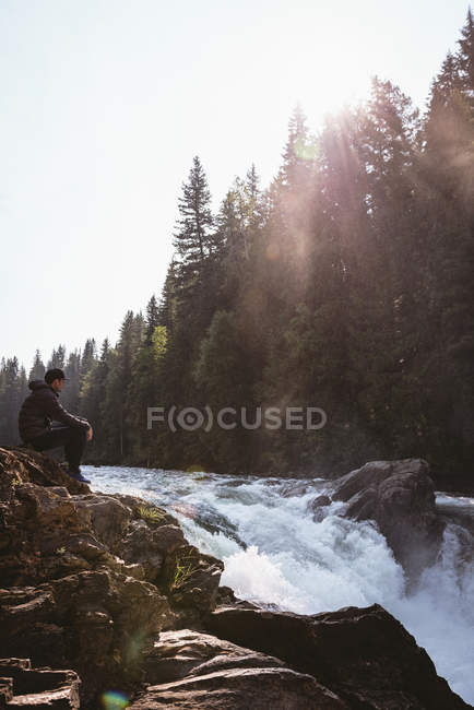 Mann sitzt an einem sonnigen Tag auf einem Felsen in der Nähe eines Wasserfalls — Stockfoto