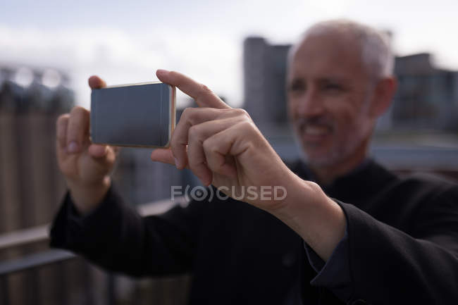 Empresario tomando fotos en el teléfono móvil en el balcón del hotel - foto de stock