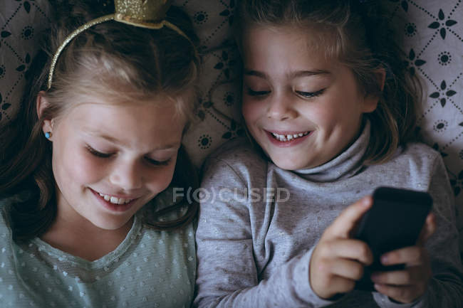 Frères et sœurs utilisant le téléphone portable sur le lit dans la chambre — Photo de stock