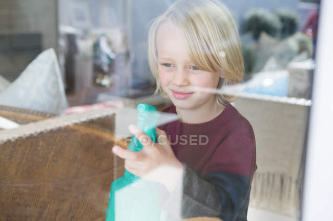 Janela de limpeza menino com frasco de spray em casa — Fotografia de Stock