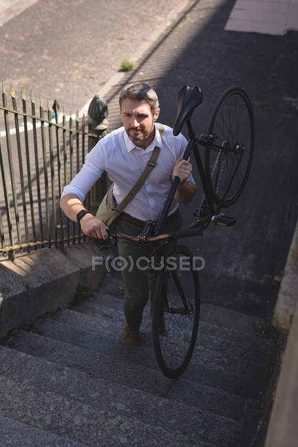 Homme portant un vélo et marchant à l'étage par une journée ensoleillée — Photo de stock