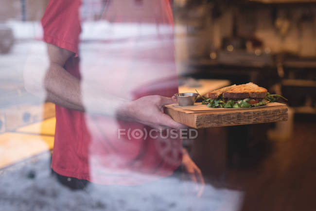 Mid section of male waiter holding sandwich in cafe — Stock Photo