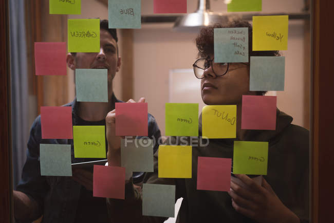 Compañeros de negocios escribiendo en notas adhesivas en la oficina - foto de stock