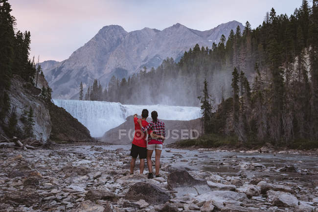 Visão traseira do casal olhando para a cachoeira — Fotografia de Stock