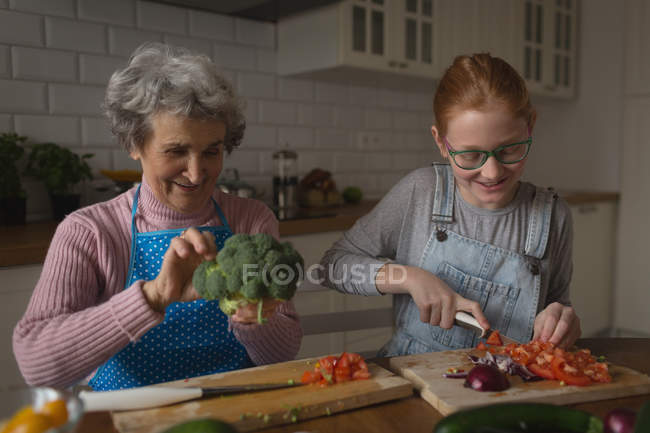 Grand-mère et petite-fille coupant des légumes dans la cuisine à la maison — Photo de stock