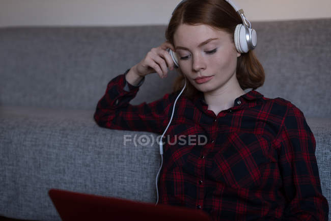 Молода жінка слухає музику зі своїм ноутбуком у вітальні — стокове фото