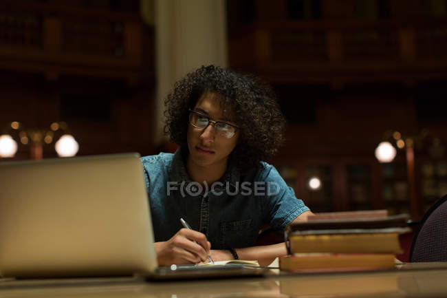 Молодий чоловік навчається з ноутбуком у бібліотеці — стокове фото