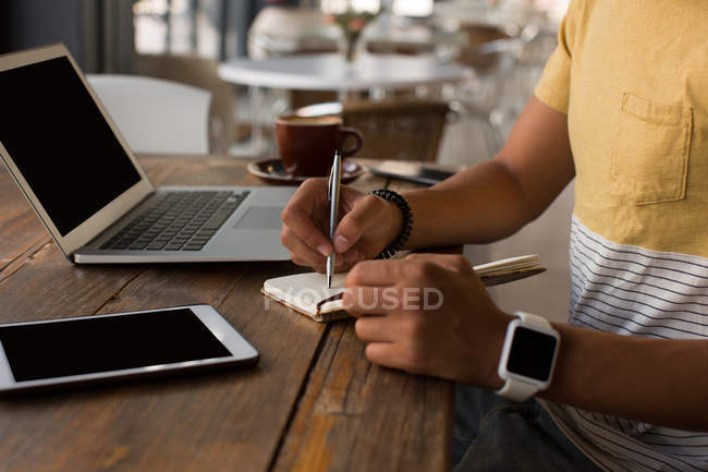 Mid section of man writing on a diary in caferetia — Stock Photo