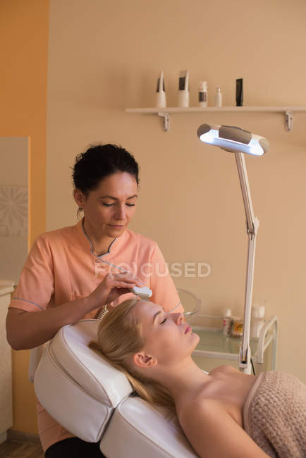 Beautician using ultrasonic scrubber on female customer in parlour — Stock Photo