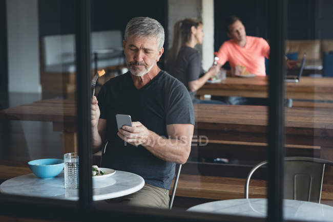 Businessman using mobile phone while having breakfast in office — Stock Photo