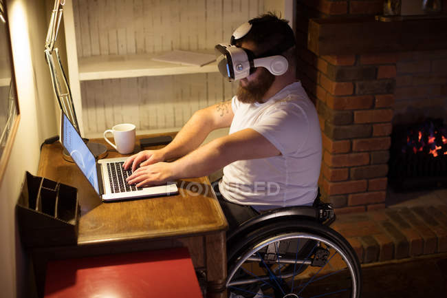 Disabled man in virtual reality headset using laptop at home — Stock Photo