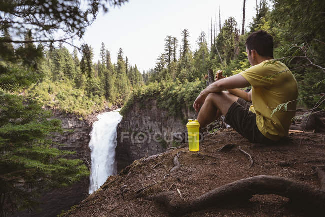 Чоловік сидить біля водоспаду в сонячний день — стокове фото