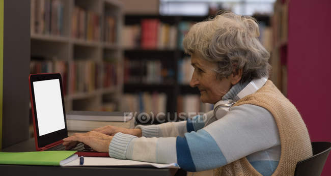 Mulher sênior ativa usando laptop na biblioteca — Fotografia de Stock