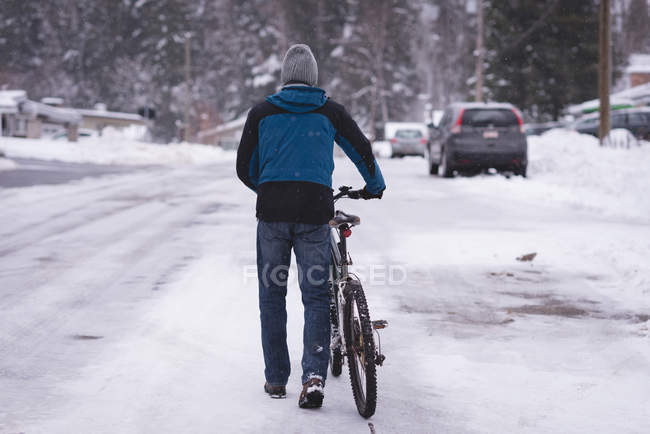 Вид сзади на человека, идущего на велосипеде по снежной улице — стоковое фото