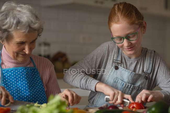 Бабушка и внучка режут овощи на кухне дома — стоковое фото