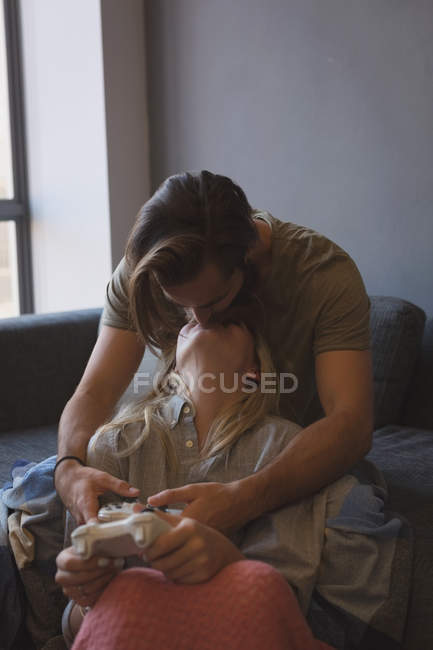 Pareja besándose mientras juegan videojuegos en casa - foto de stock