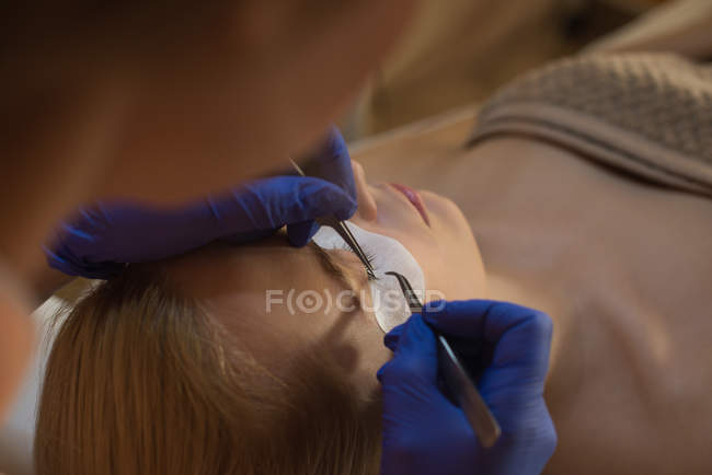Beautician giving eyelash extension treatment to female customer in parlour — Stock Photo