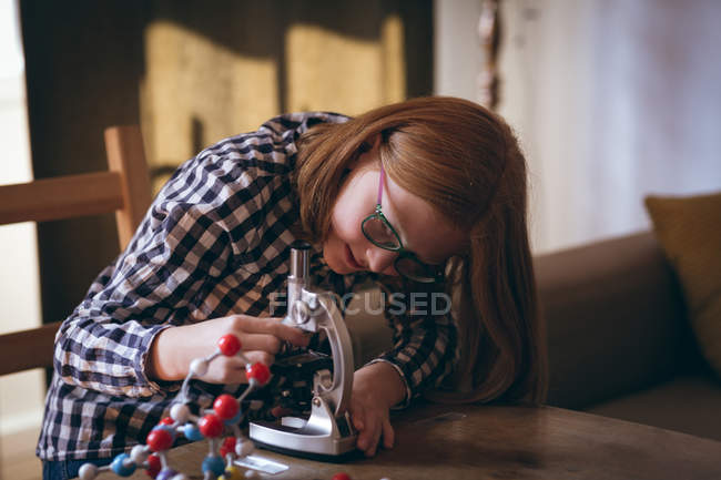 Девушка делает эксперимент на микроскопе дома — стоковое фото
