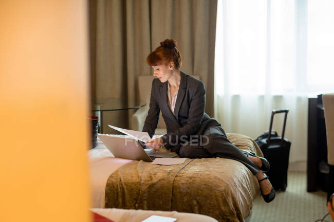 Donna d'affari che guarda documenti su un letto in camera d'albergo — Foto stock