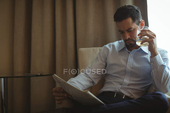 Бизнесмен читает газеты, выпивая виски в гостиничном номере — стоковое фото