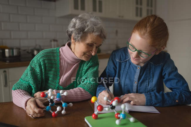 Grand-mère aider petite-fille avec des devoirs dans la cuisine à la maison — Photo de stock