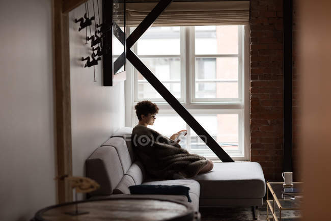 Женщина пользуется цифровым планшетом, отдыхая дома на диване — стоковое фото