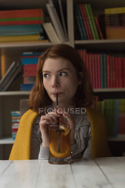 Mujer tomando jugo de limón con paja en la sala de la biblioteca - foto de stock