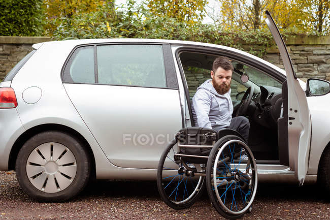 Инвалид молодой человек с инвалидной коляской во время посадки в машину — стоковое фото