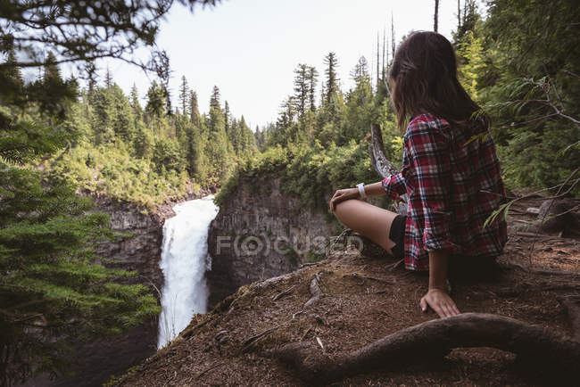 Вид сзади на женщину, сидящую у водопада — стоковое фото